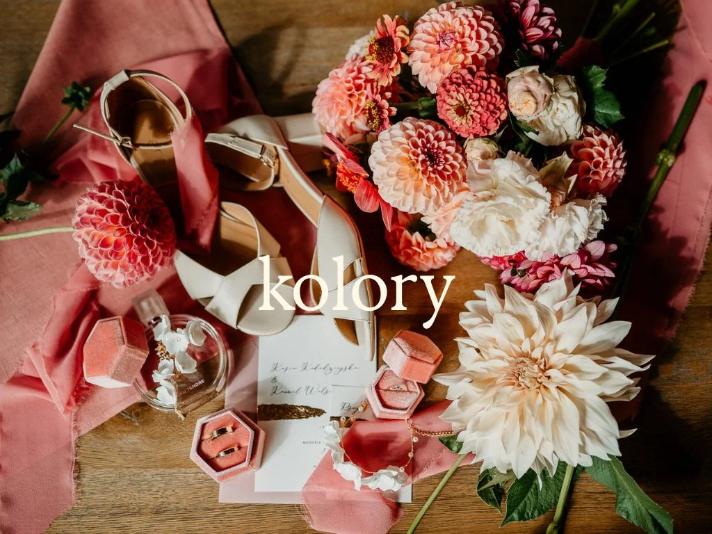 Flat lay of pink, peach, and white dahlias and roses, pink shoe, jewelry, and pink wrapping paper on a wooden surface, with text "kolory" overlaying the image.