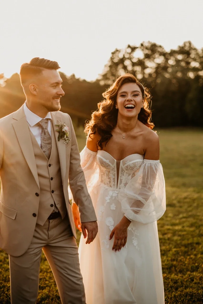 A happy bride and groom holding hands outdoors during sunset, with trees in the background.
