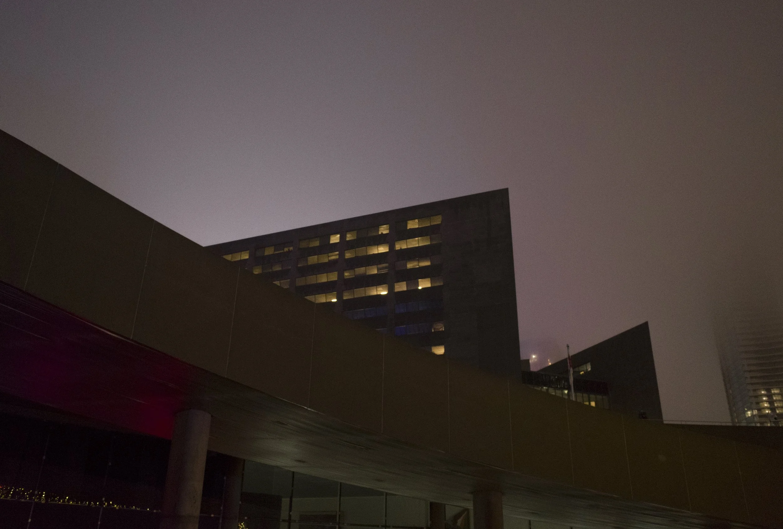 Night view of modern buildings with illuminated windows against a dark, foggy sky.