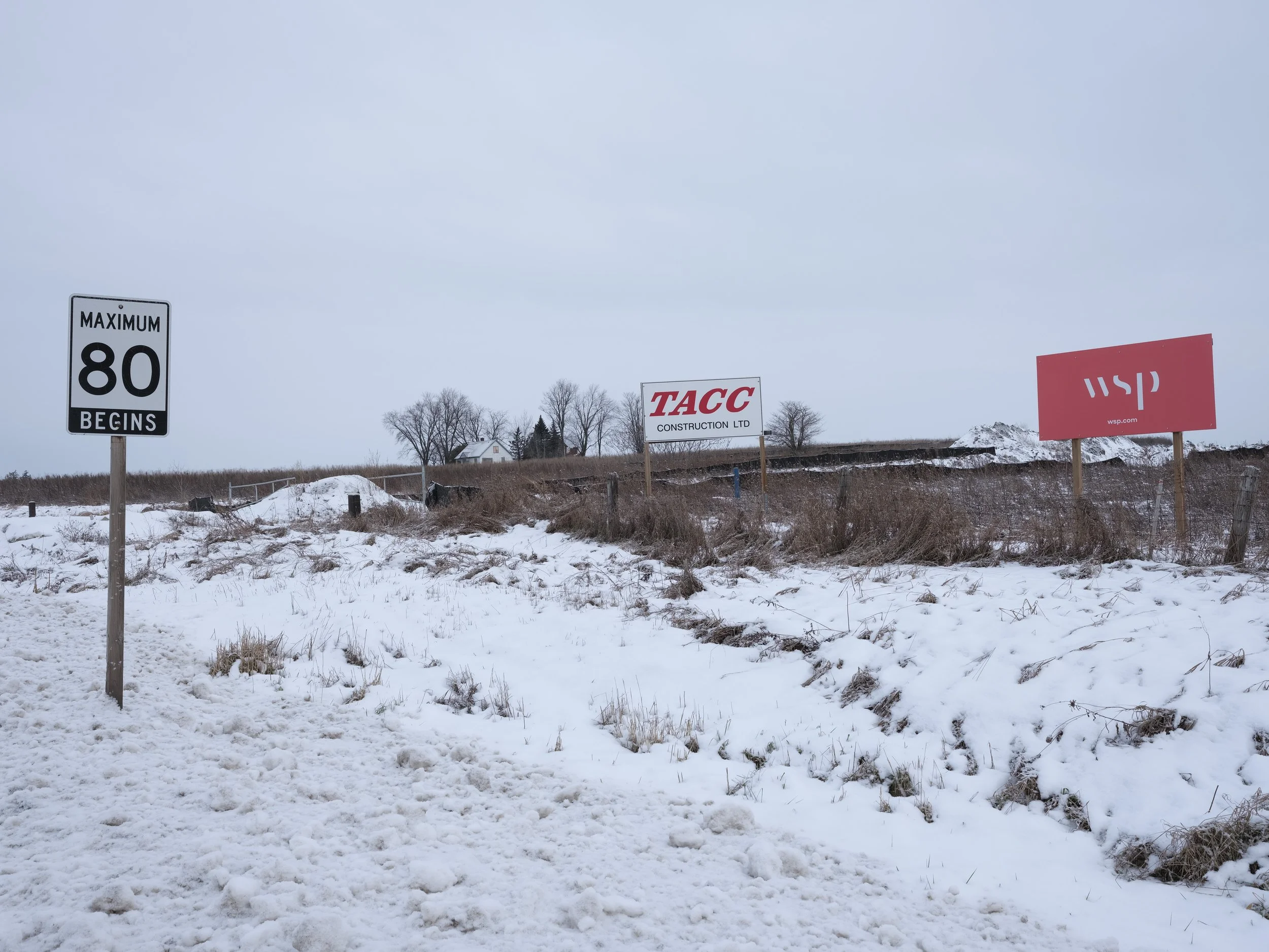 Snow-covered roadside with a sign indicating a maximum speed limit of 80 mph, and two construction company signs for TACG Construction Ltd and WSP.