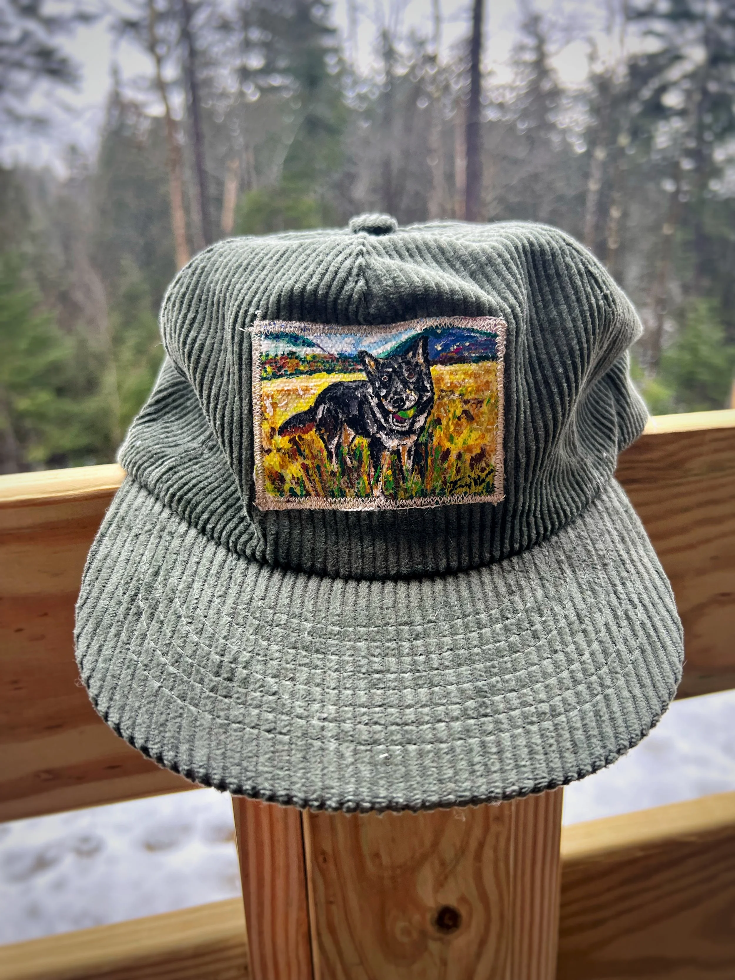 Gray corduroy cap with an embroidered patch of a black dog standing in a grassy field.