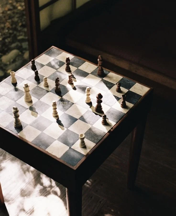 Une table en bois avec un échiquier contenant des pièces d'échecs en plastique, dans une pièce éclairée par la lumière naturelle représentant notre logo en damier et la stratégie qu'il y a autour du jeux, étant la base de nos métiers
