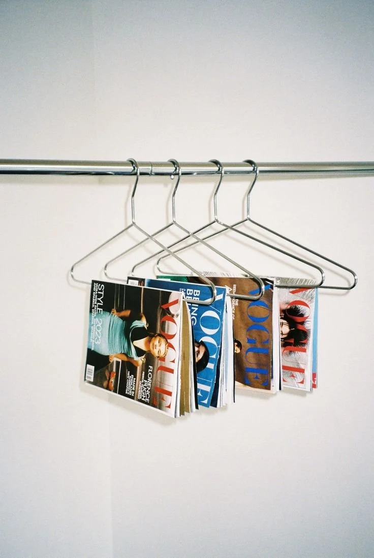 Cinq cintres en métal suspendus sur une tringle, chaque cintre tenant un magazine Vogue.