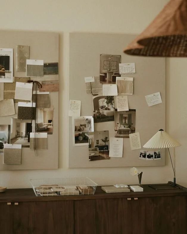 Une décoration intérieure avec deux panneaux d'affichage remplis de photos et de notes, un meuble en bois avec une boîte en fil métallique, des livres, une lampe de bureau à abat-jour en papier et un grand abat-jour suspendu en tissu au plafond.