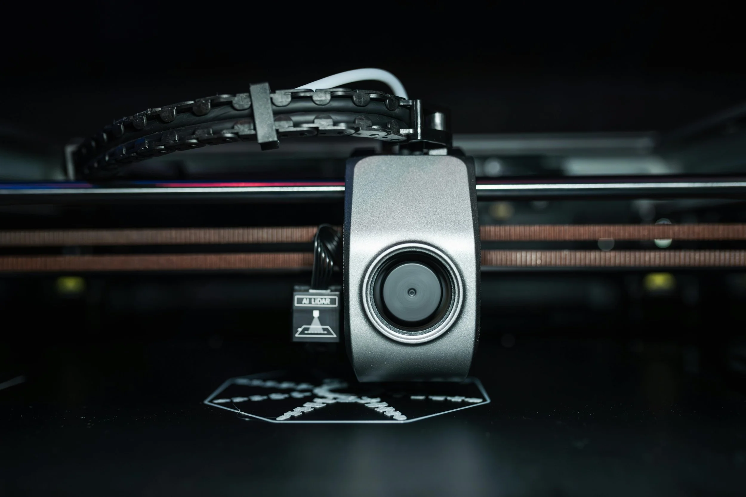 Close-up of a 3D printer's extruder printing on a black surface.