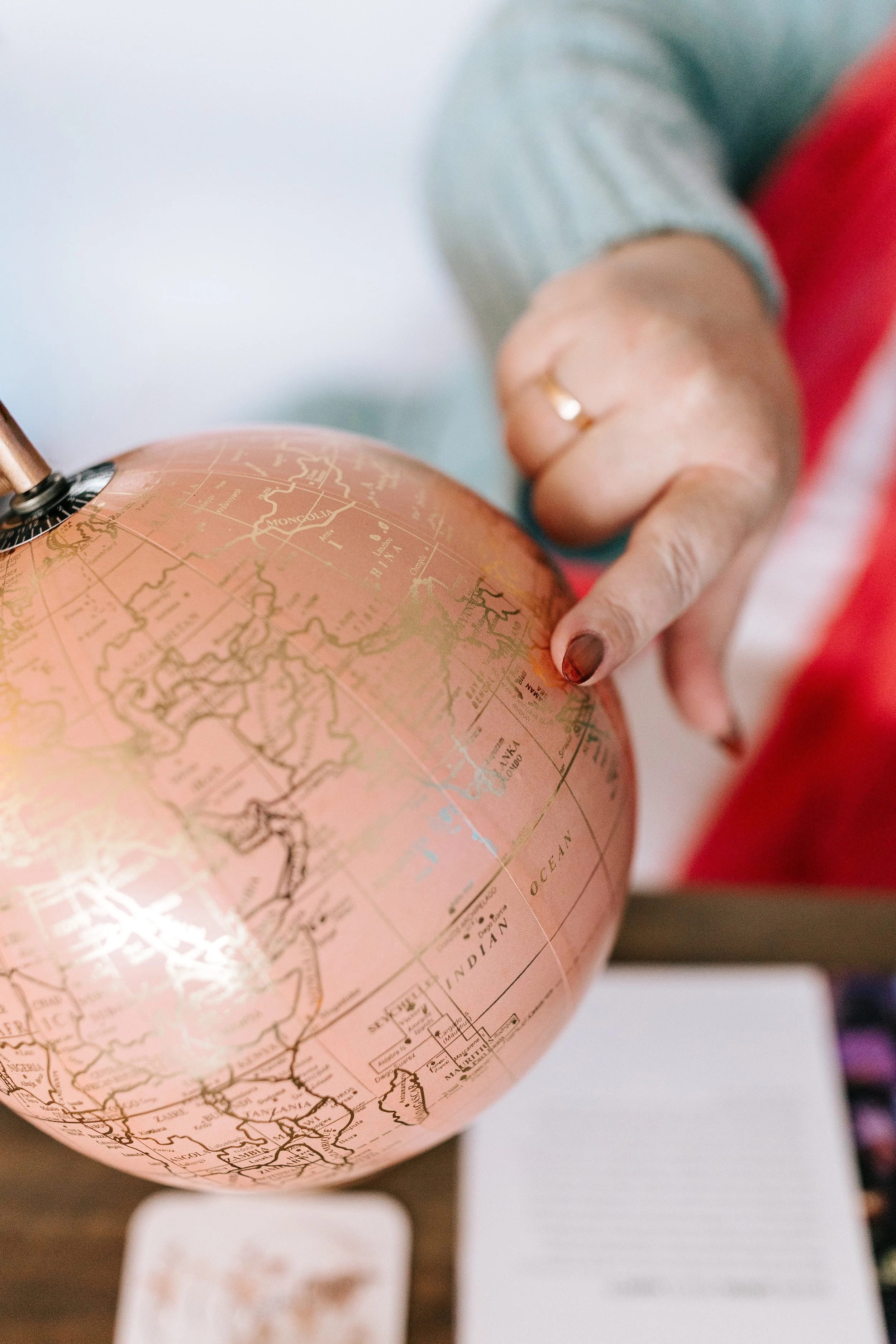Person pointing at a pink globe with a world map, focusing on continents and oceans.