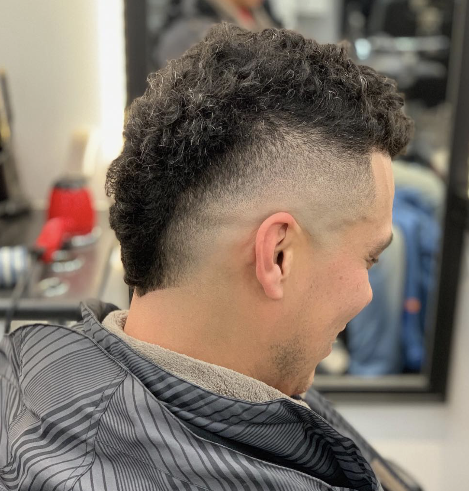 Side view of a man with a fresh fade haircut, curly dark hair on top, and shaved sides, sitting in a barber shop chair.