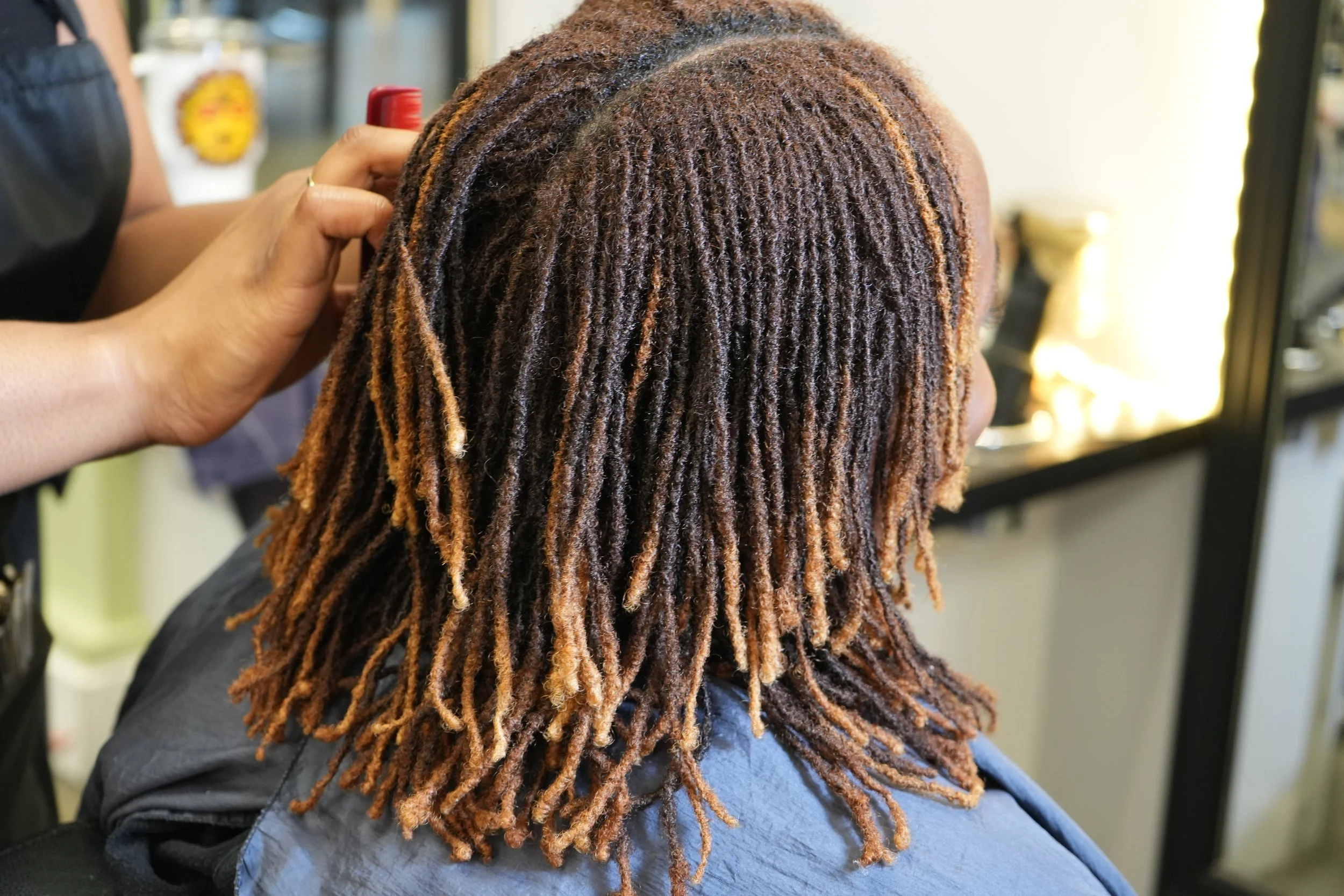 A person getting their hair styled with dreadlocks at a salon.