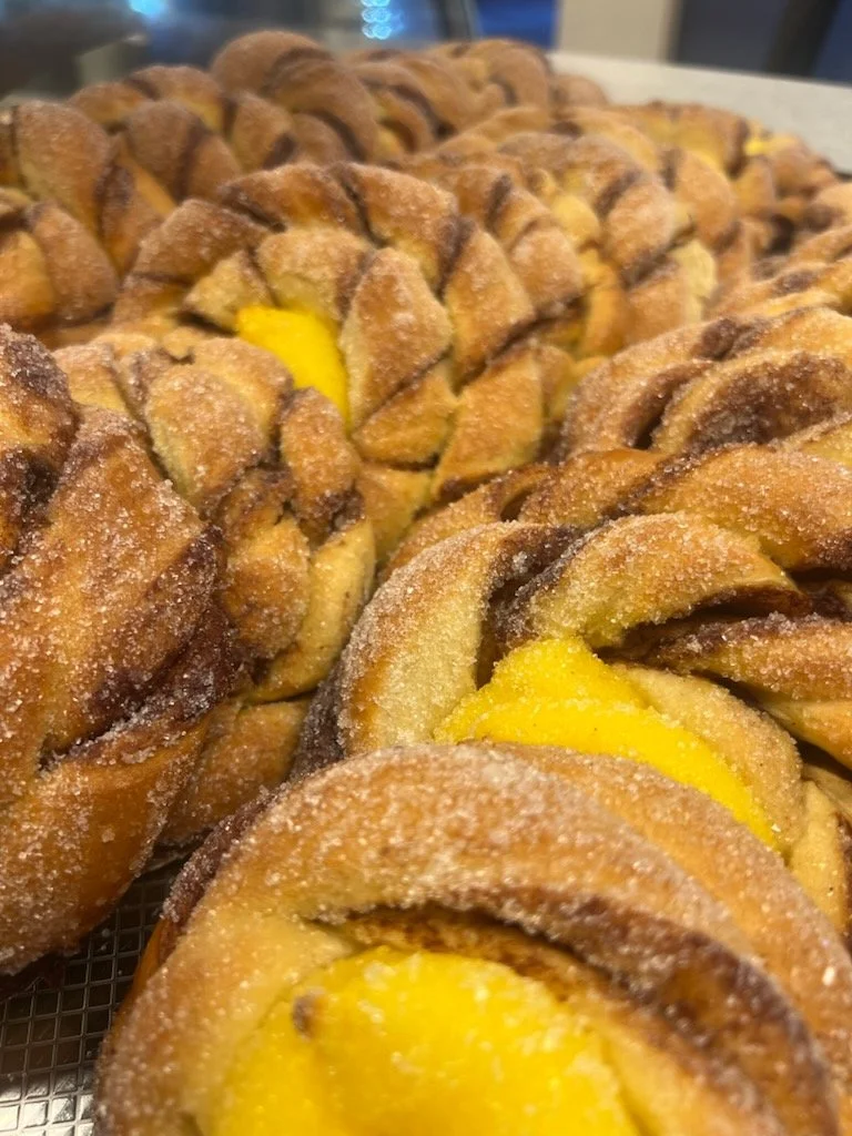 Nærbilde av flere kryssende kanelboller med sukker, fylt med vaniljekrem, utstilt på et brett.