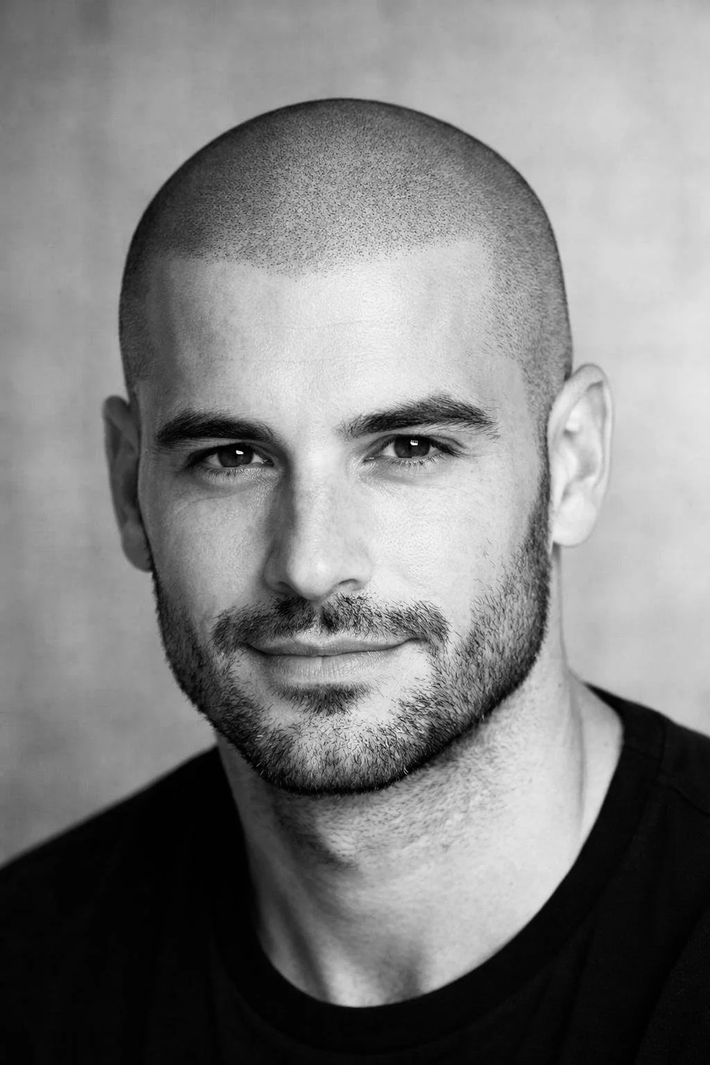 Ritratto di un uomo con testa rasata, barba curata, sorriso leggero, vestito con maglietta nera,
testa rasata con effetto realizzato con la tricopigmentazione a Bolzano