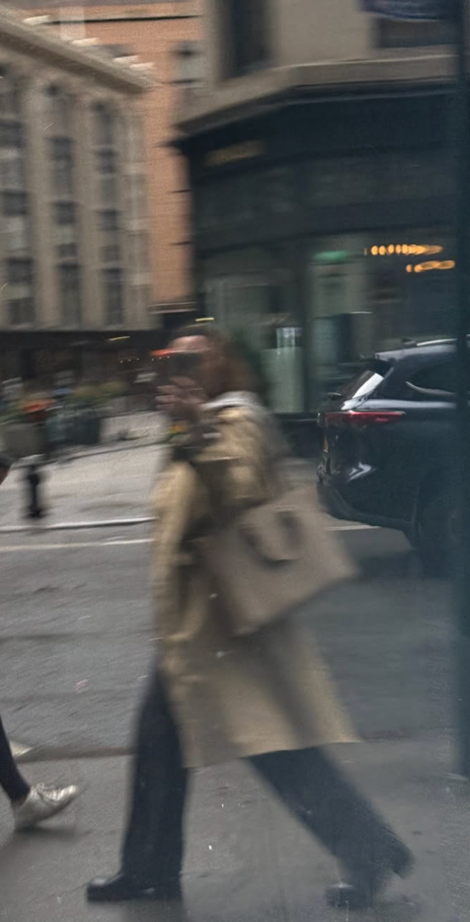 Blurred reflection of a person walking on a city street, taking a photo, with buildings and cars in the background.