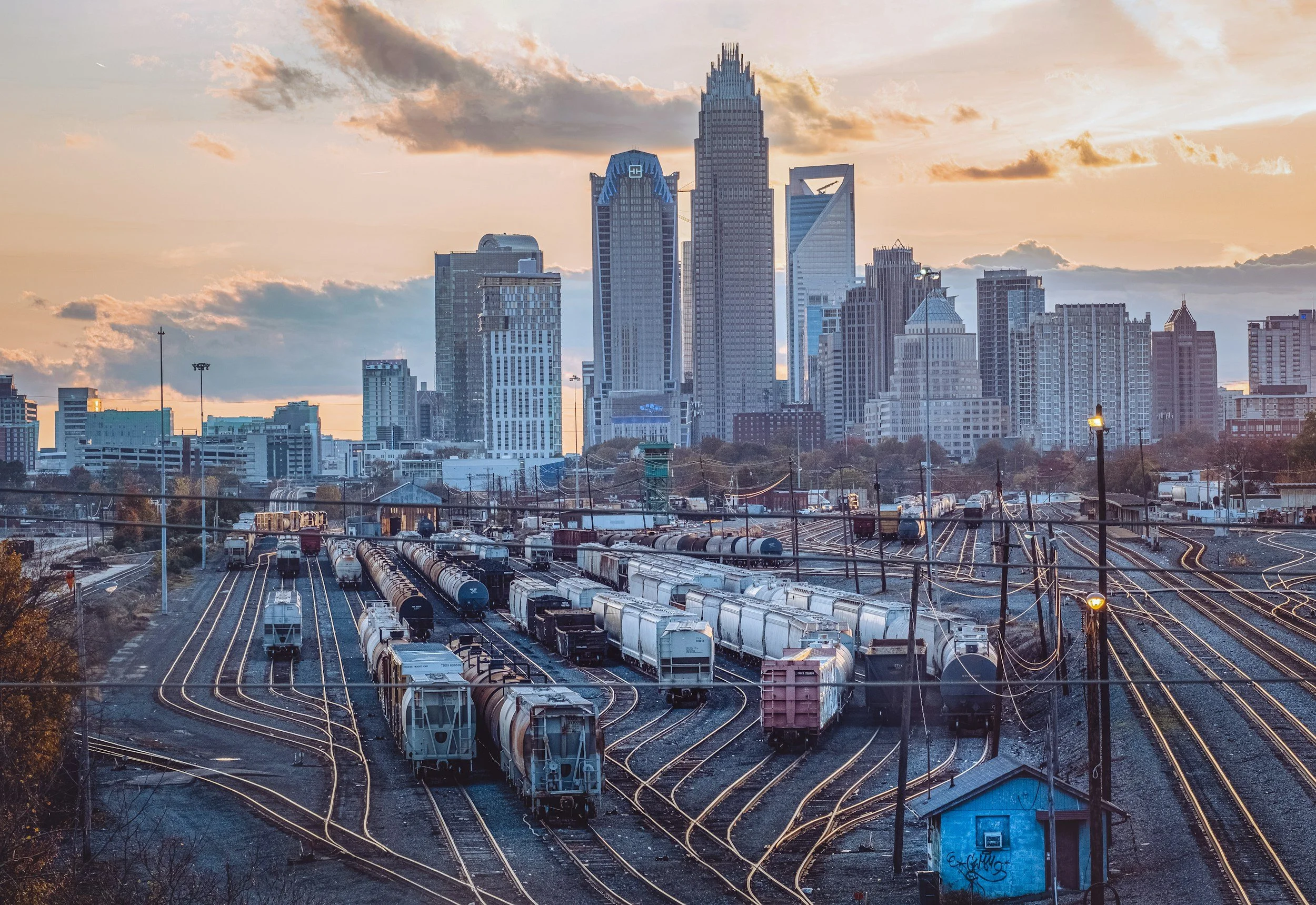 City skyline with tall skyscrapers at sunset and train tracks in the foreground.