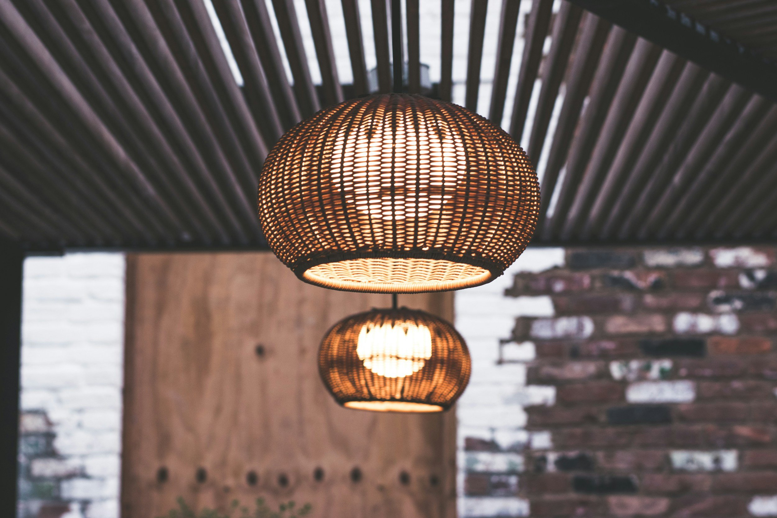 Two wicker pendant lights hanging from a ceiling in a room with a brick wall.