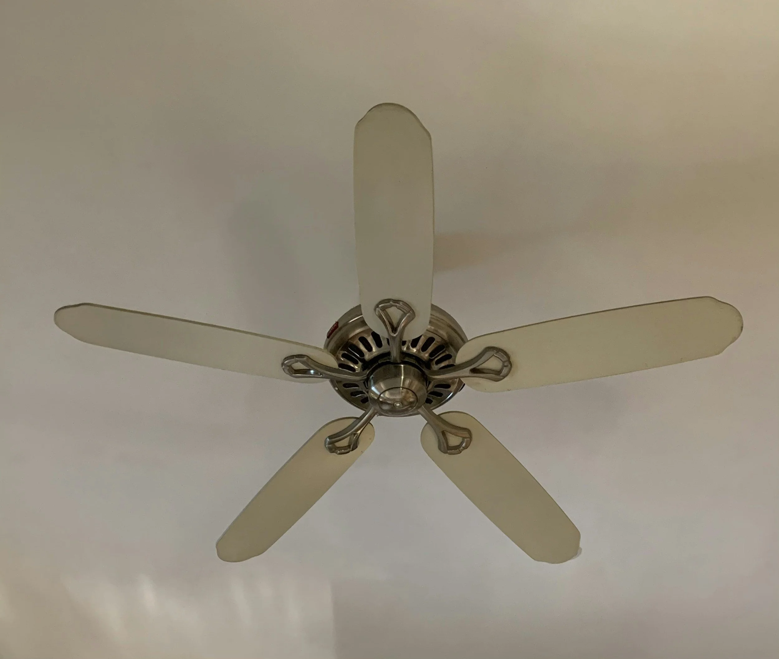 Ceiling fan with five blades and a metallic central hub mounted on a white ceiling.