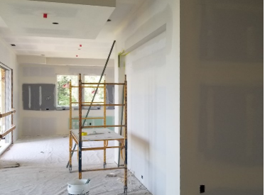 Interior of a room under construction, with scaffolding and a paint roller on the floor.