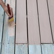 Person painting wooden deck with light blue paint using a brush.