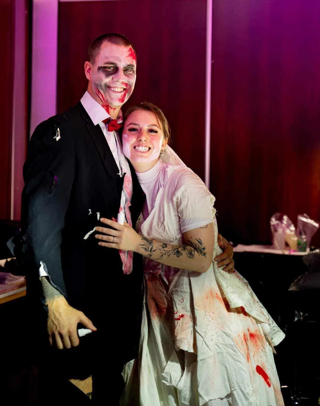 Deux personnes déguisées en zombies, souriantes et maquillées de manière effrayante, lors d'une fête d'Halloween ou d'une soirée costumée.