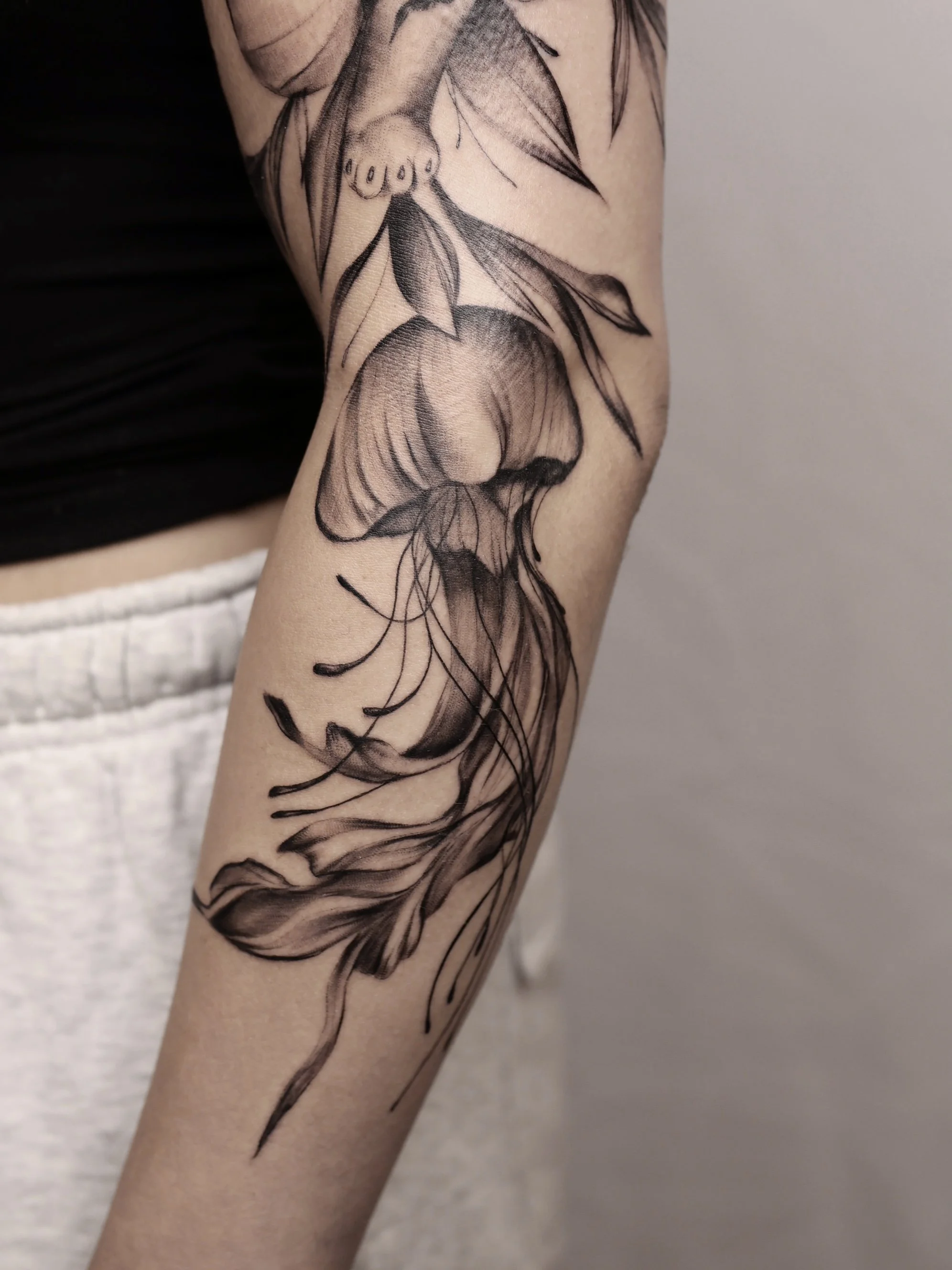 Tatouage en noir et gris d'une méduse, représentant ses tentacules et son corps, sur le bras d'une personne.
