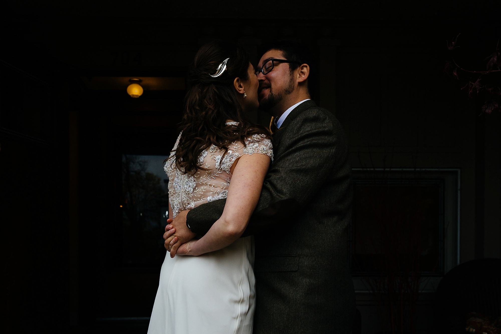 A bride and groom sharing an intimate moment indoors, with the bride wearing a lace wedding dress and the groom in a dark suit, both smiling