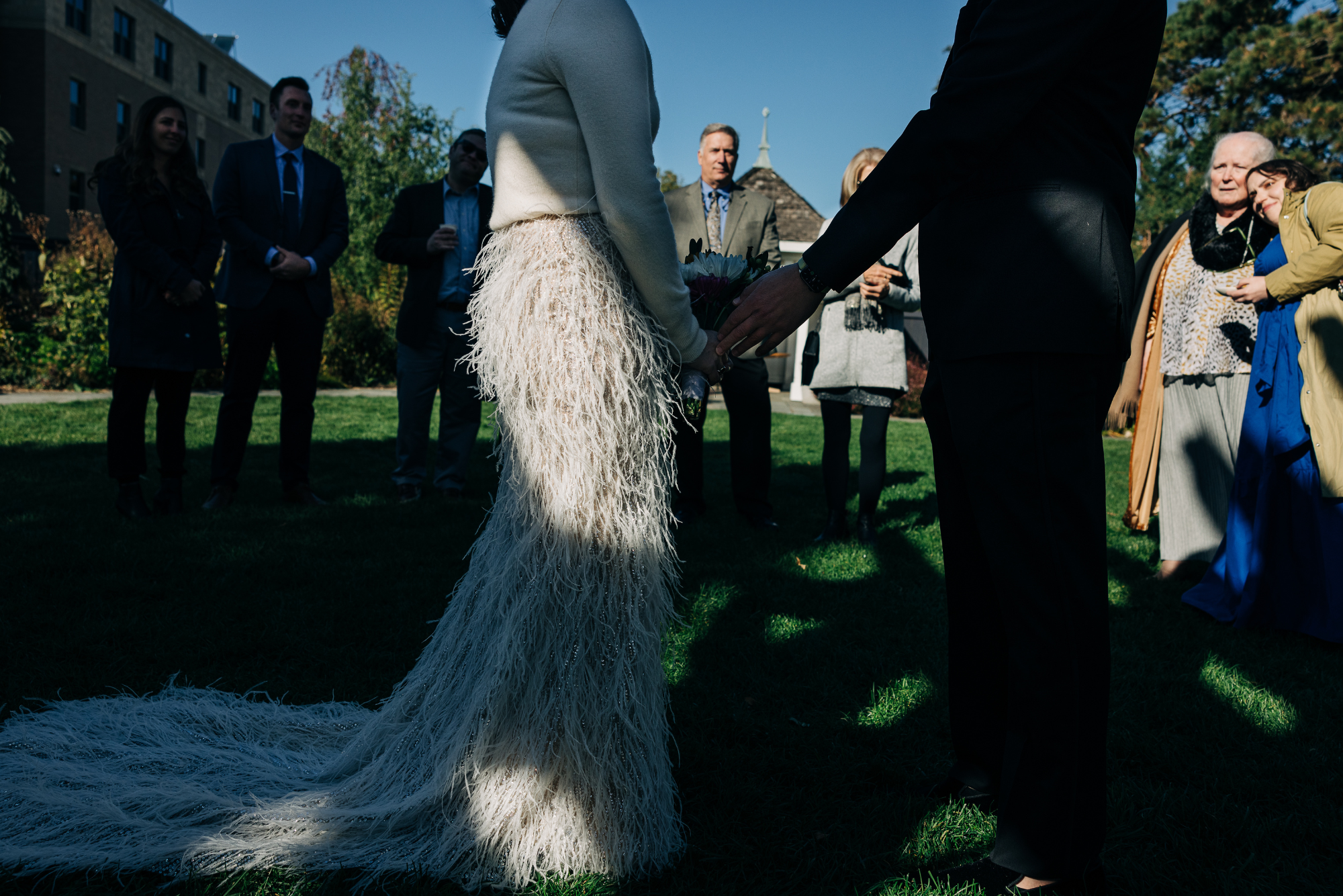 A couple holding hands during their outdoor wedding ceremony, surrounded by friends and family.