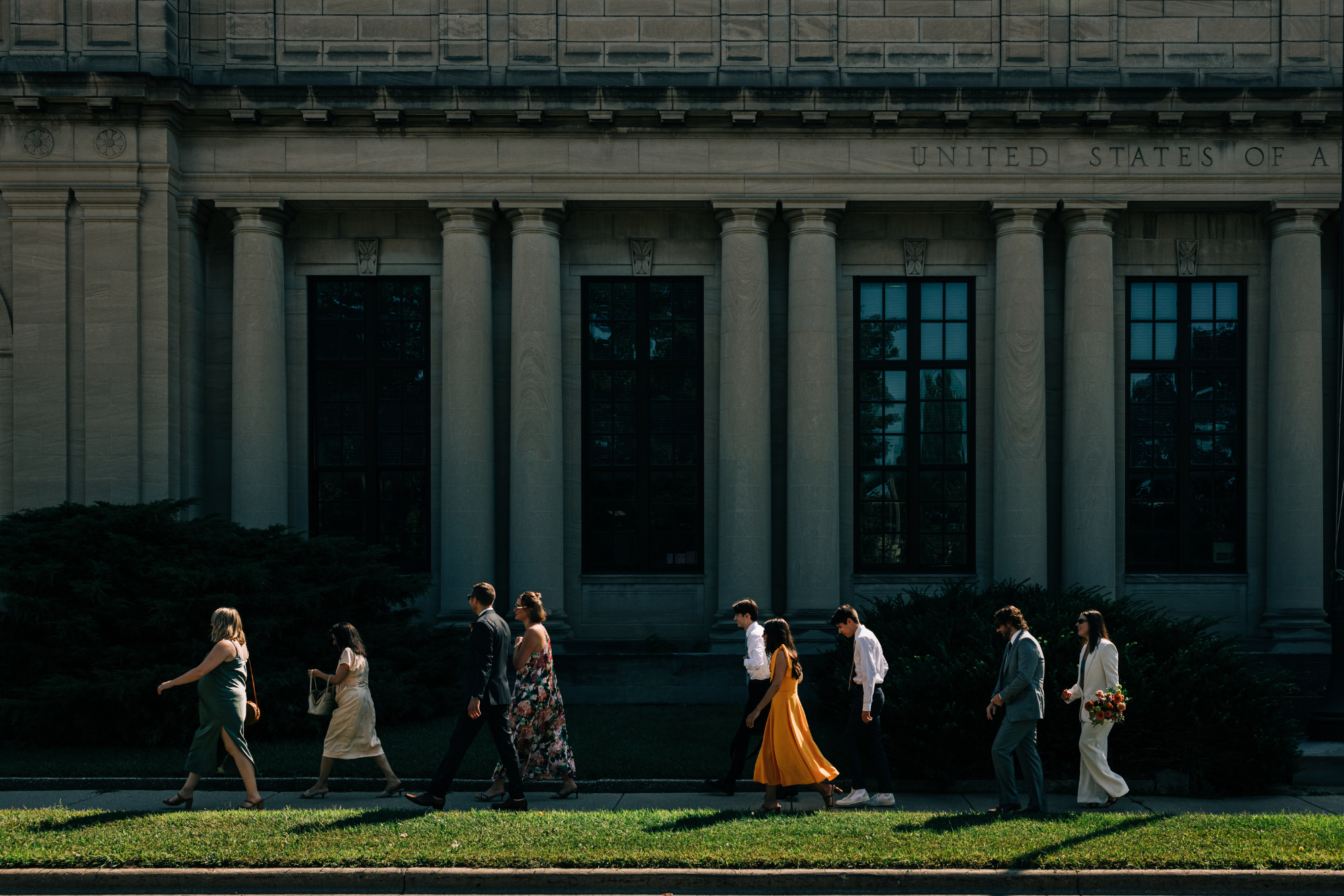 A group of people walking in front of a classical-style building with columns, possibly during a formal event or ceremony.