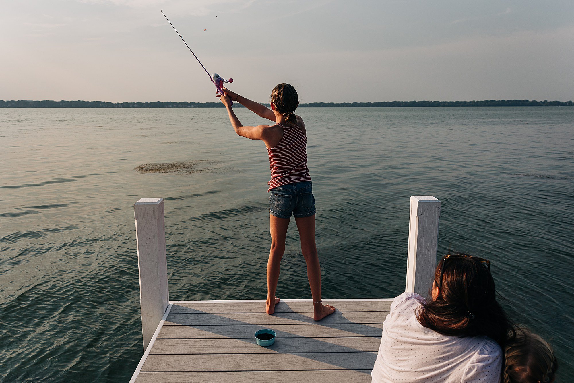 teen girl casts fishing line into the lake while mom watches