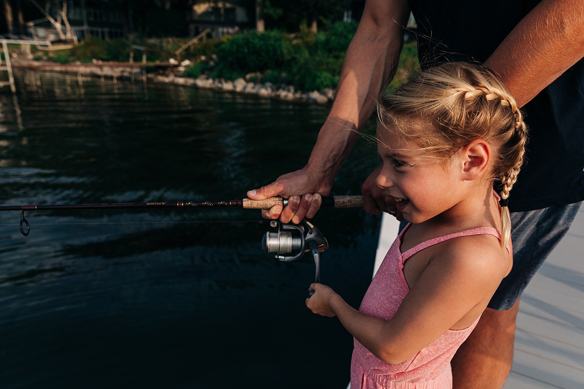 mom helps daughter hold fishing pole over lake water