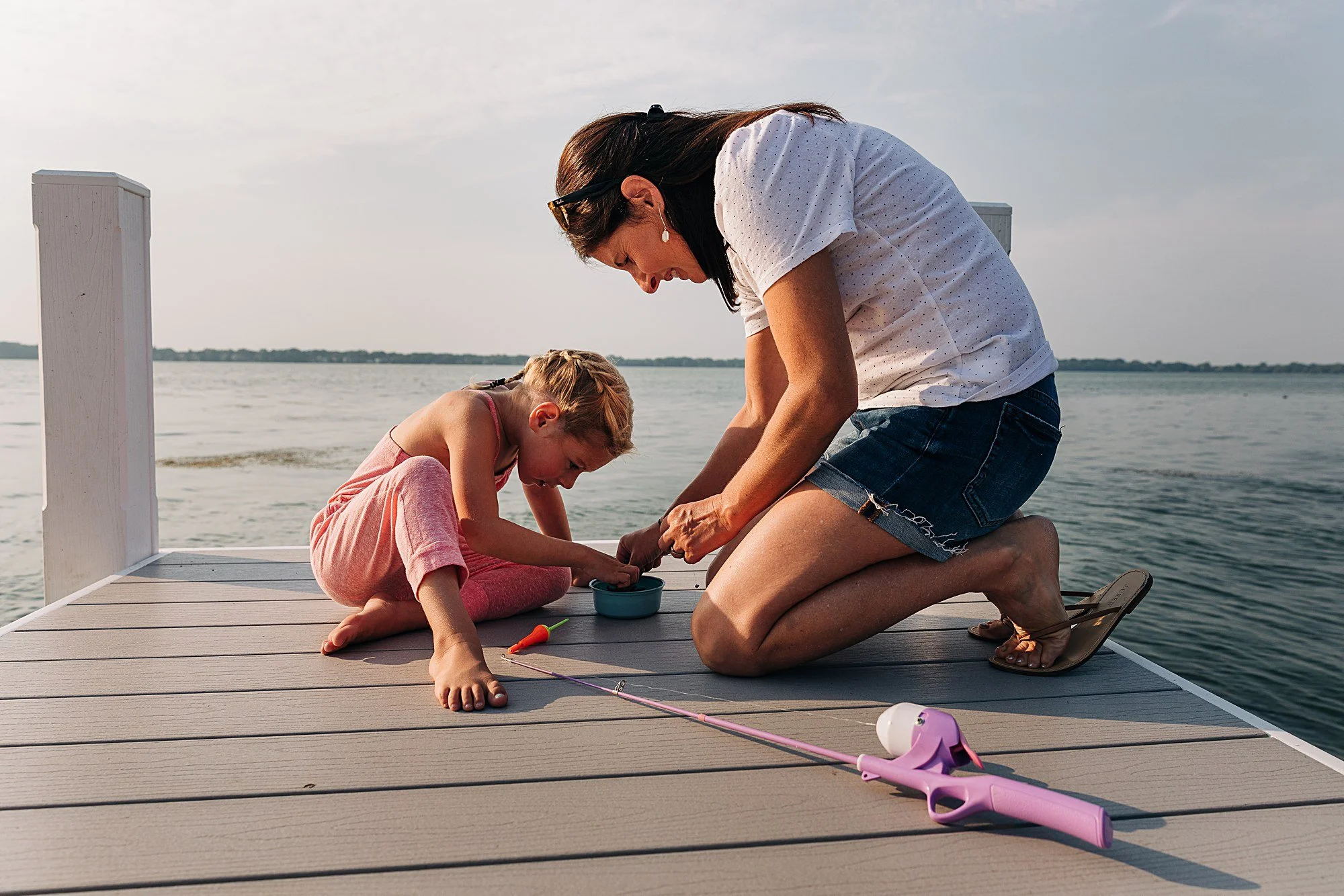 Mom helps daughter with putting worm on a hook for fishing rod