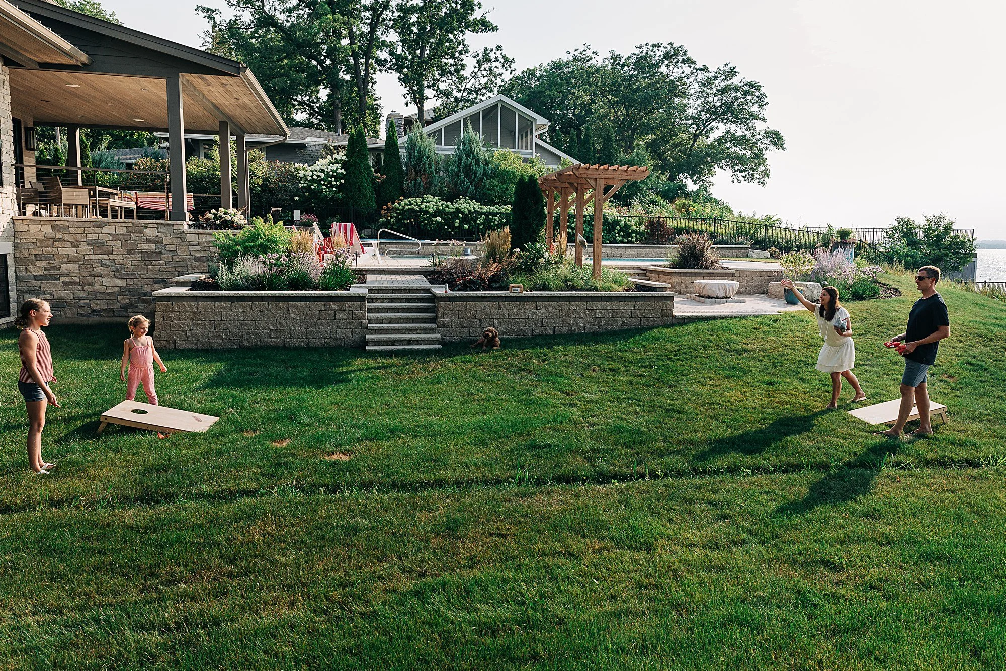 family of four plays corn hole game in backyard
