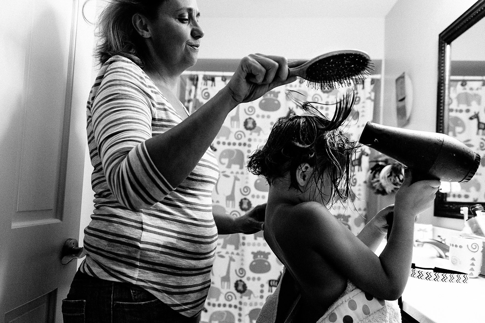 A woman blow drying a young child's wet hair in a bathroom.