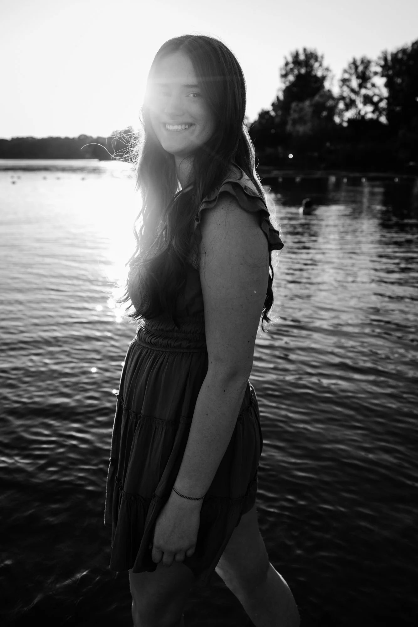 A young woman standing in a body of water during sunset, smiling at the camera.