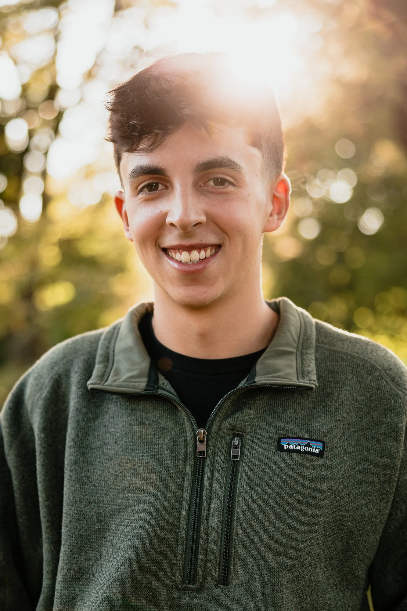 Young man smiling outdoors during sunset, wearing a green Patagonia fleece jacket.