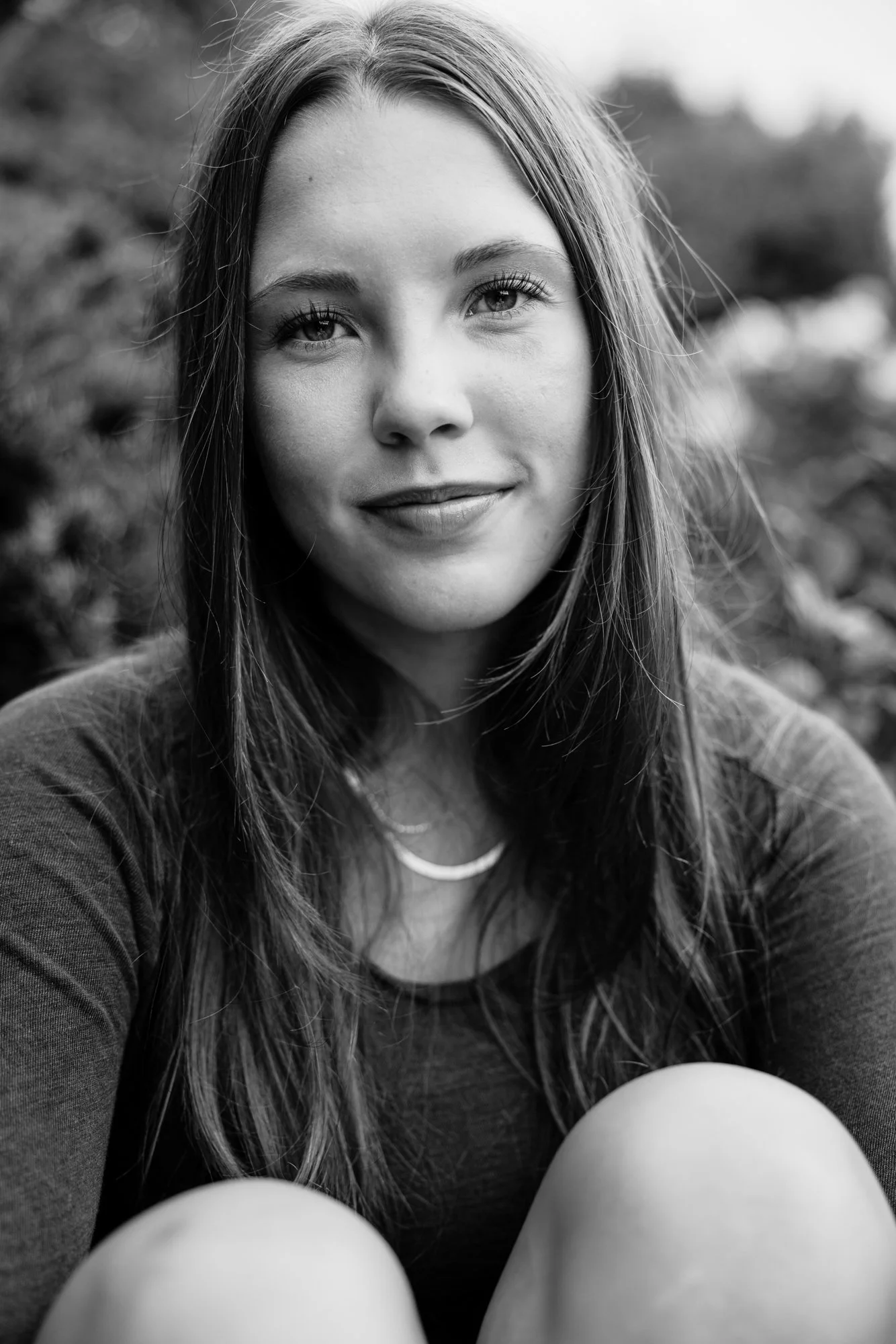 A young woman with long hair, smiling, outdoors in black and white.