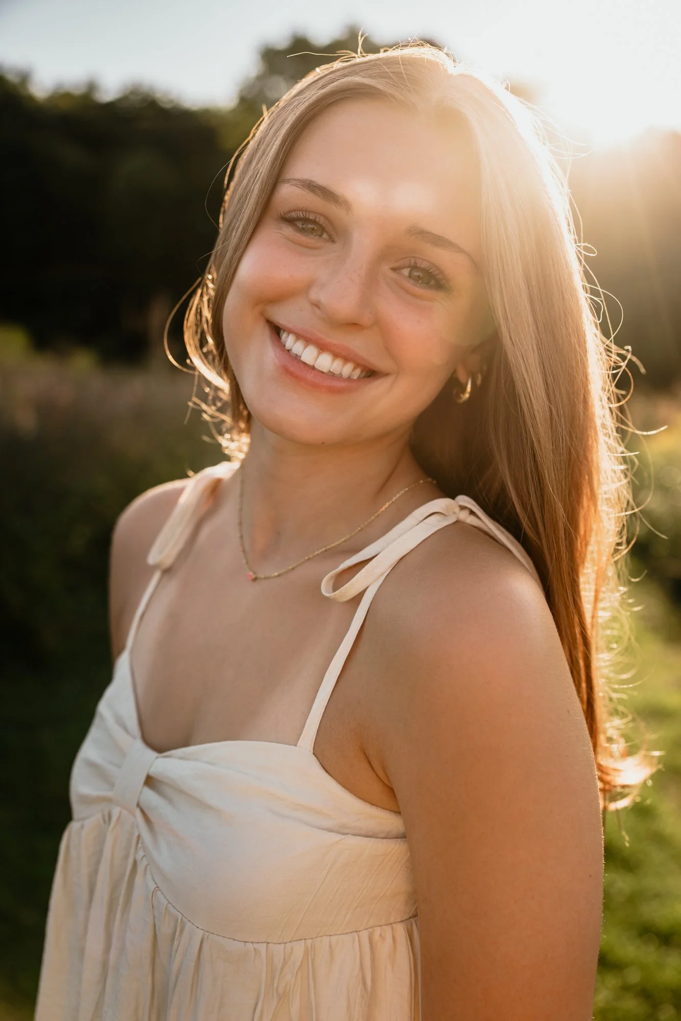 A young woman with red hair smiling outdoors at sunset.