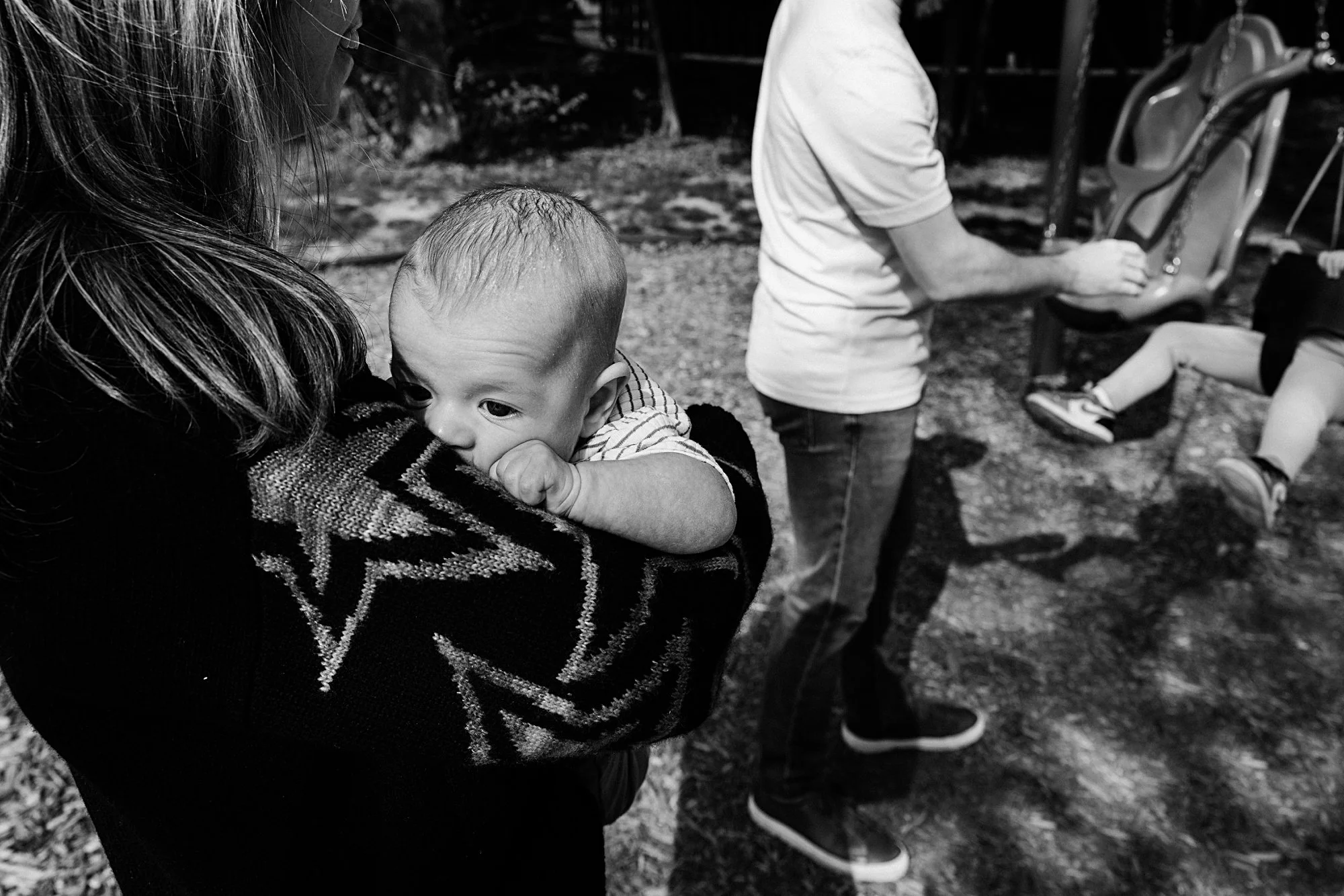 A woman holding a young child near a playground at night.