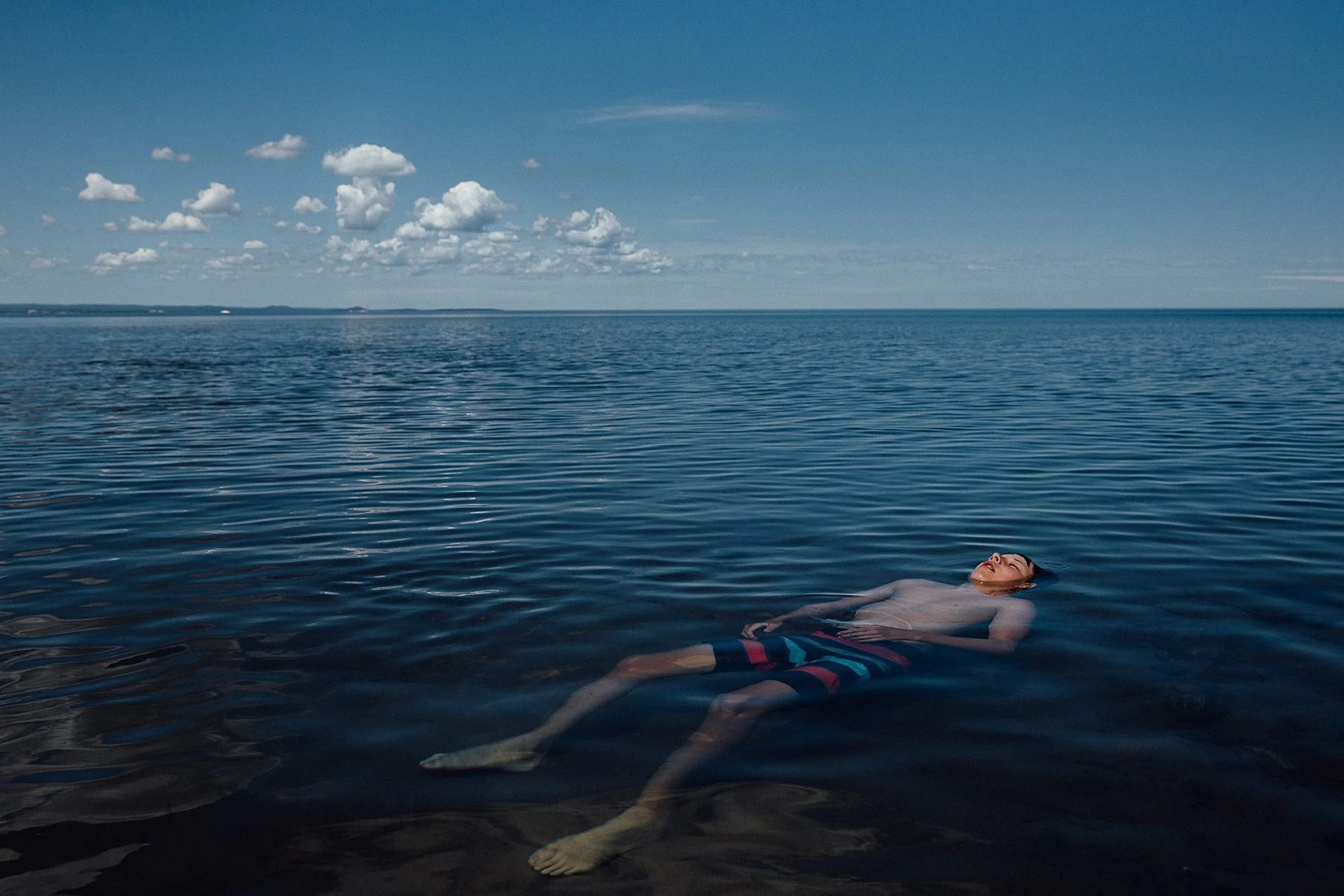 A person floating on their back in a calm body of water under a blue sky with scattered clouds.