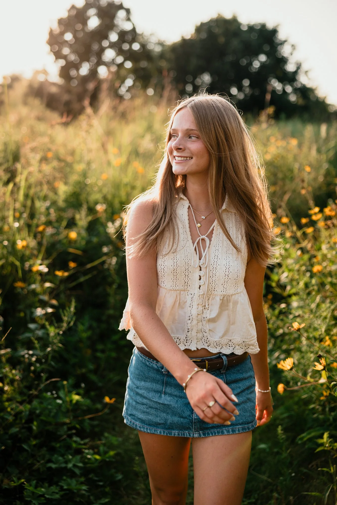 Young woman smiling and walking in a field of yellow flowers at sunset