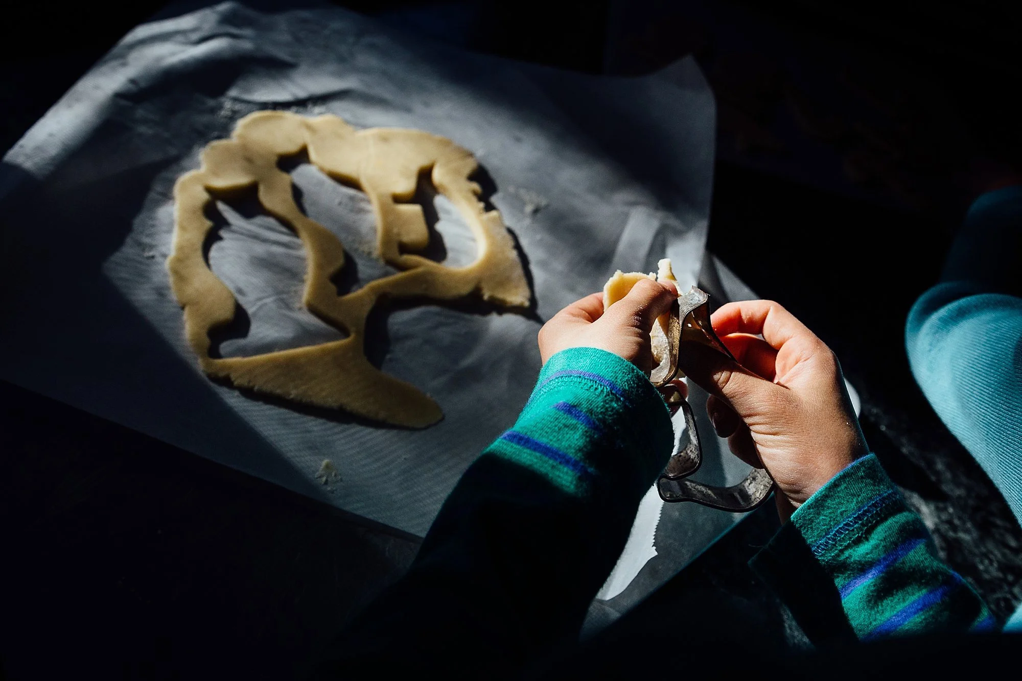 A person using a cookie cutter to cut cookie dough shaped like a human face.
