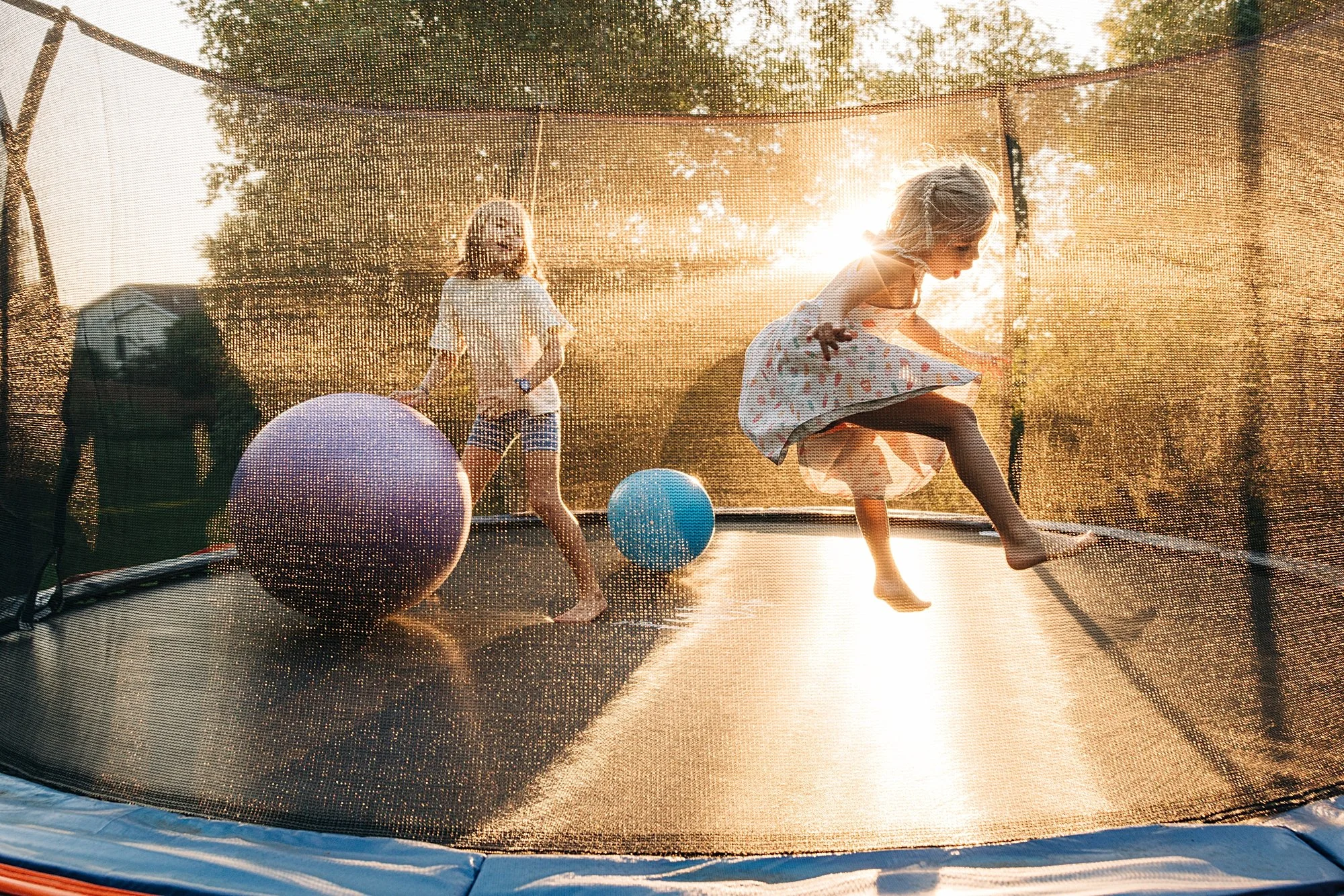 Two young girls playing on a trampoline with exercise balls during sunset.