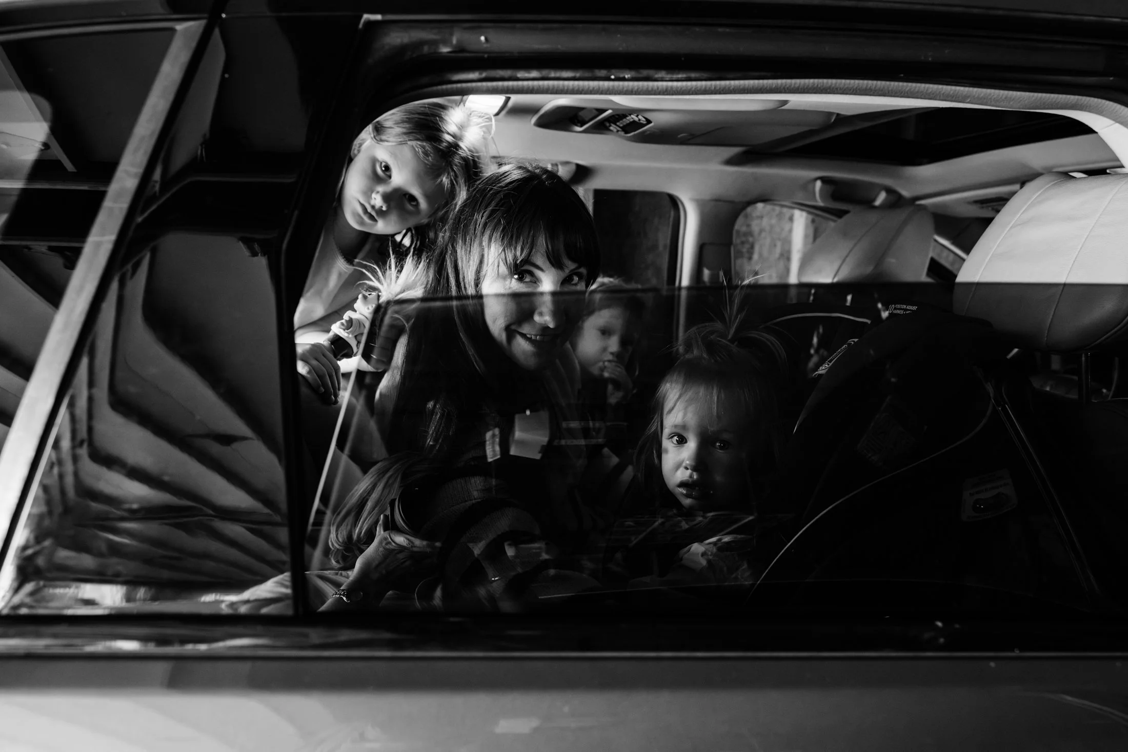 View of a smiling woman and four children inside a vehicle, looking through the rear window. The photo is in black and white.