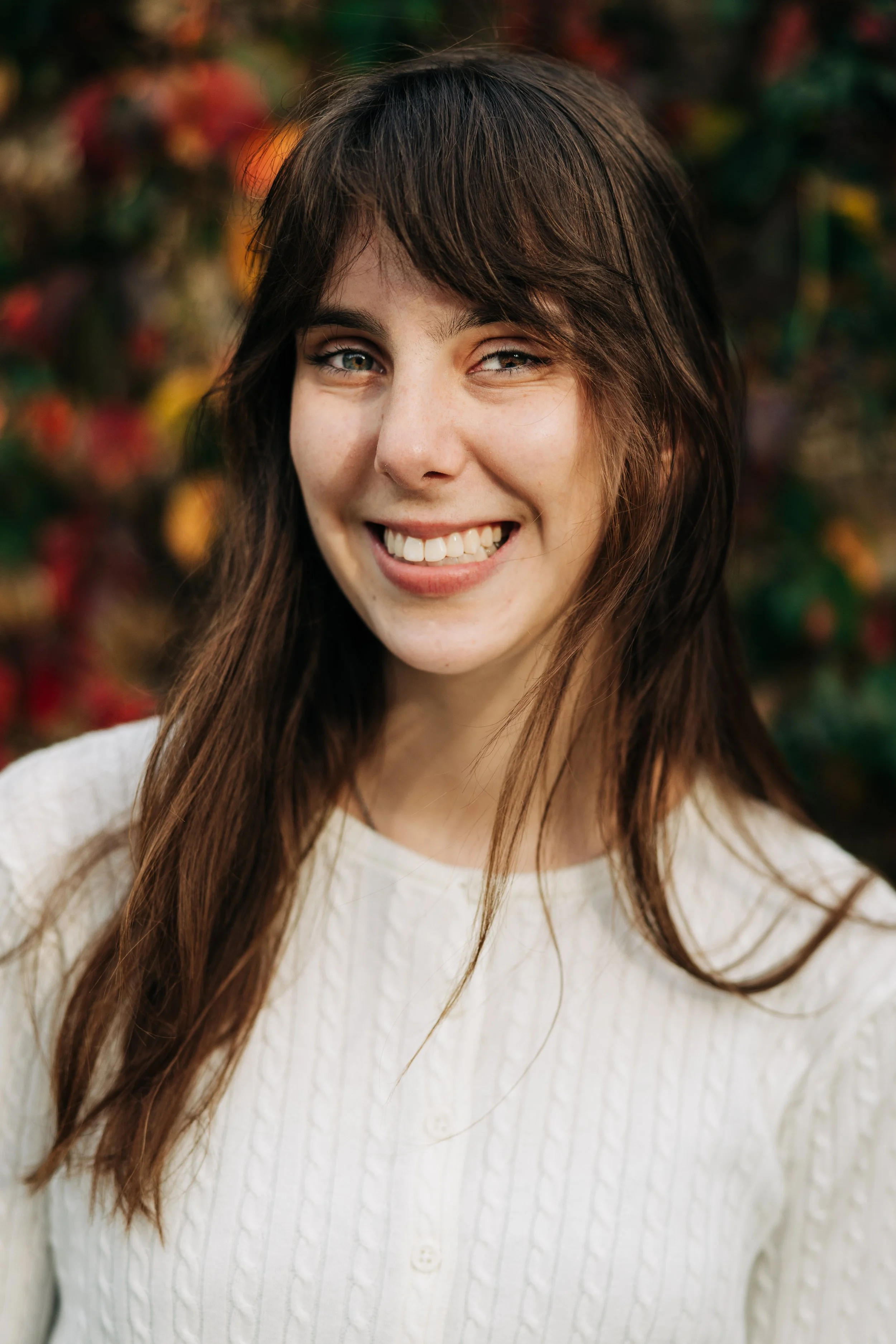 Young woman smiling, outdoor background with colorful autumn leaves.