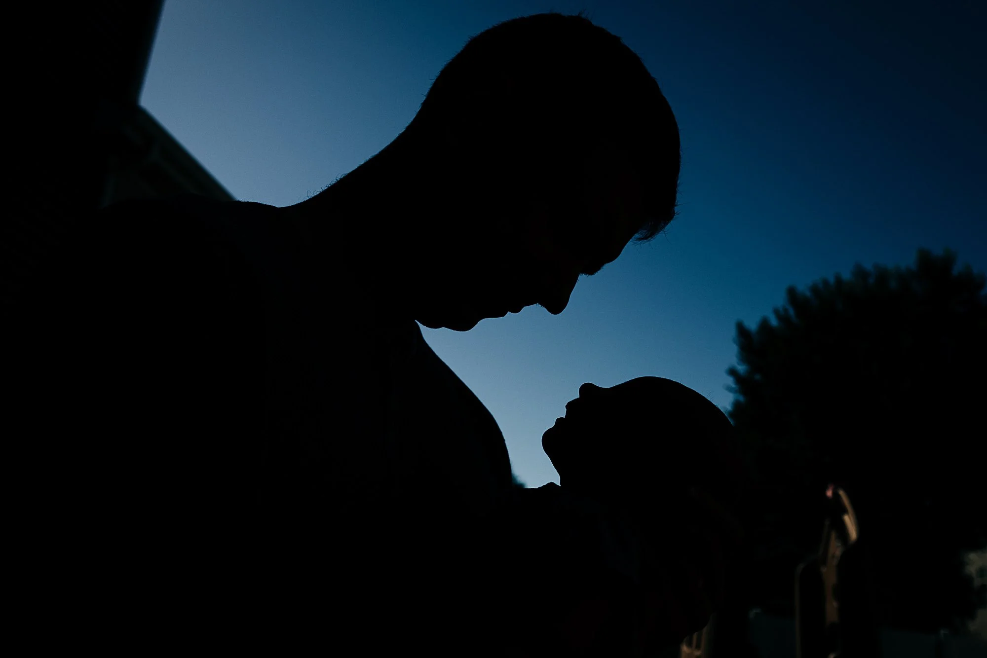Silhouette of a man looking down at a child during dusk with trees in the background.