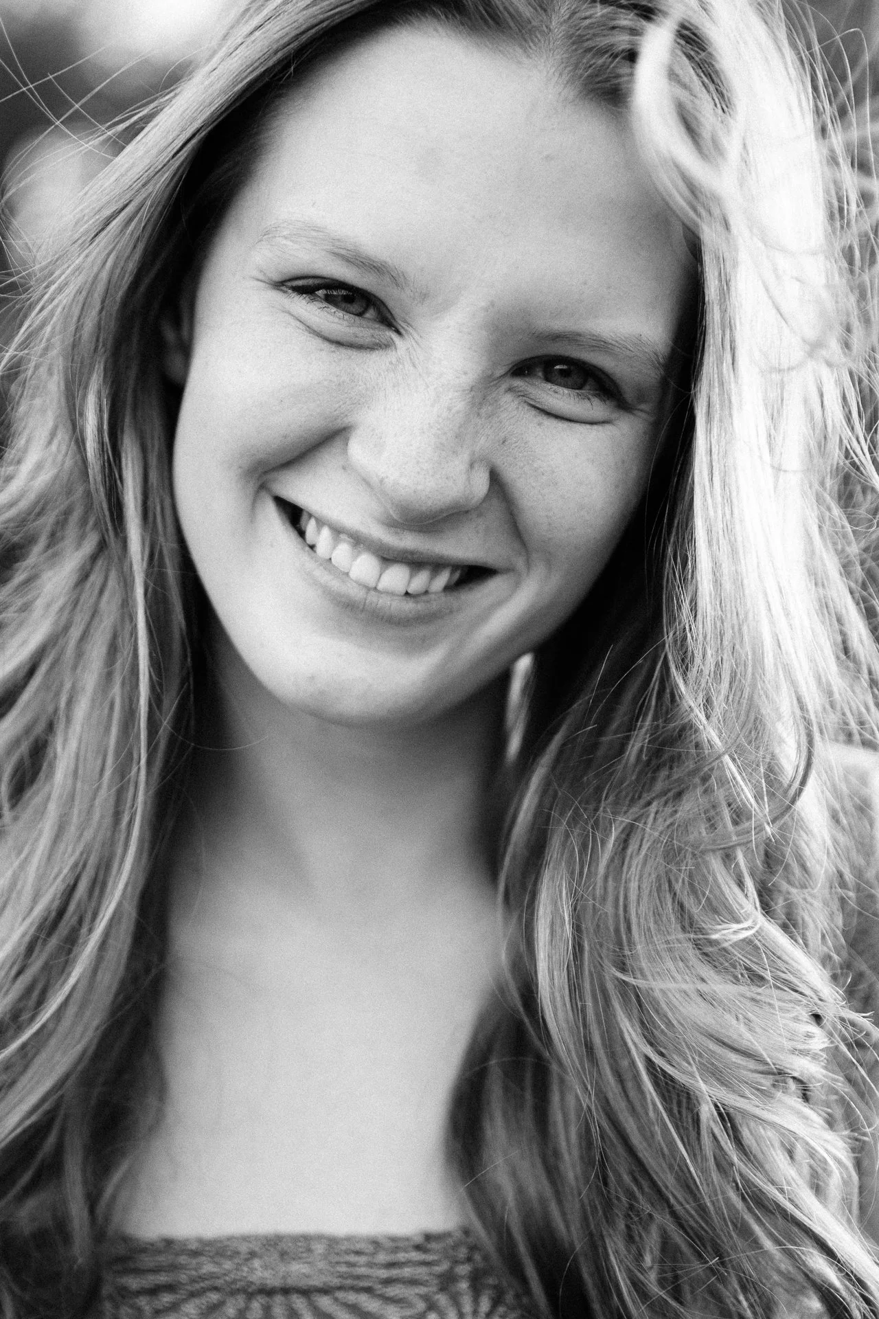 Close-up black and white photo of a young woman with long hair smiling at the camera.