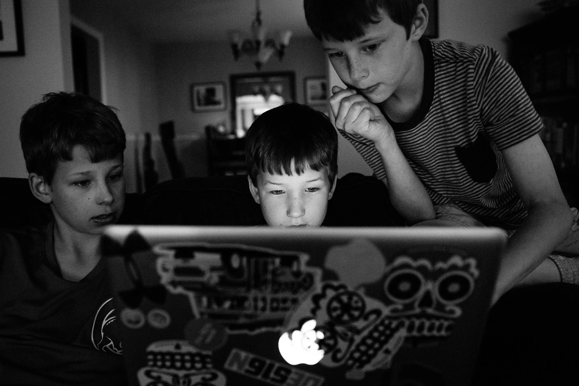 Three boys sitting on a couch, looking at a laptop screen in a dimly lit room.