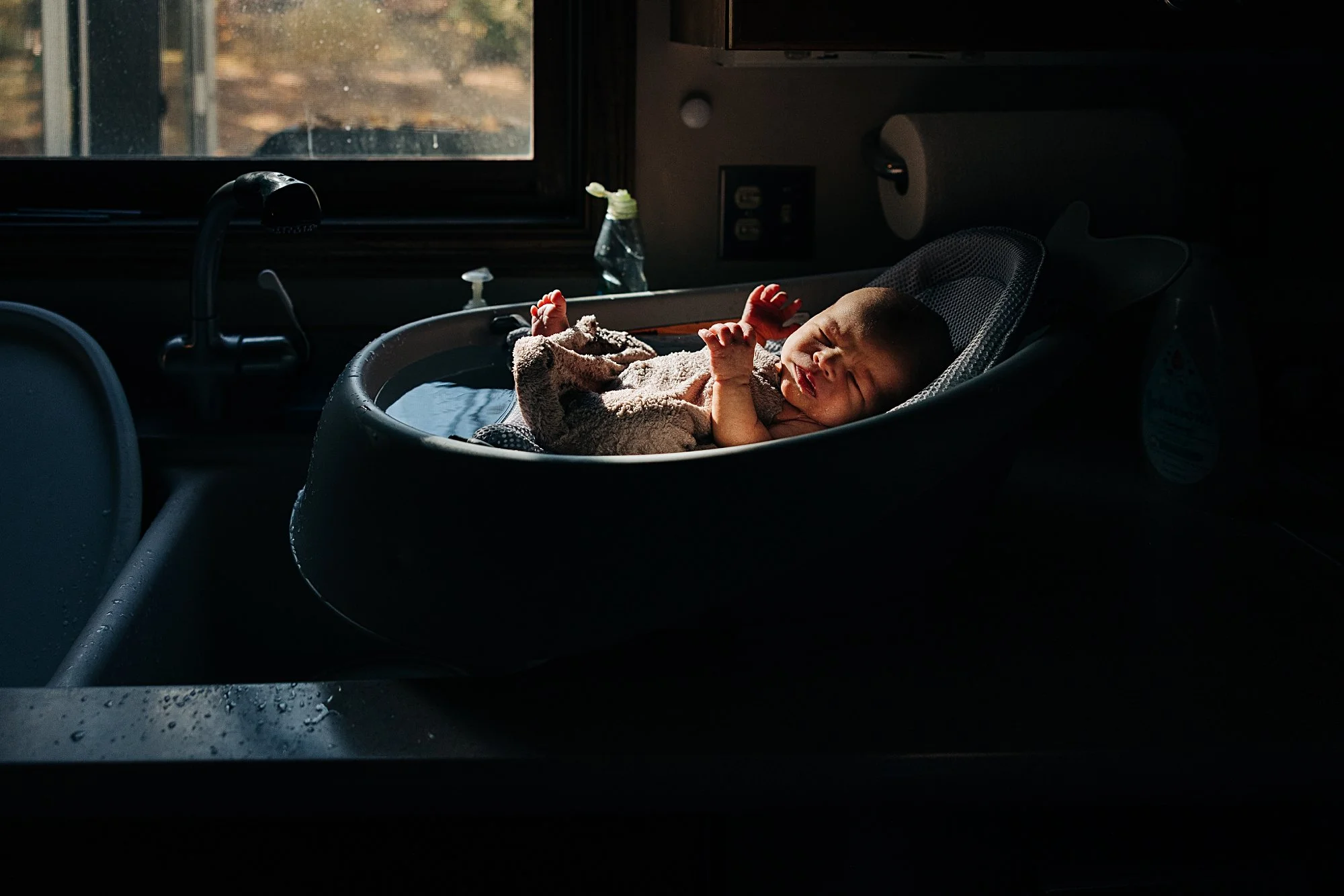A newborn baby sleeping in a car seat with sunlight illuminating their face inside a vehicle, near a window.