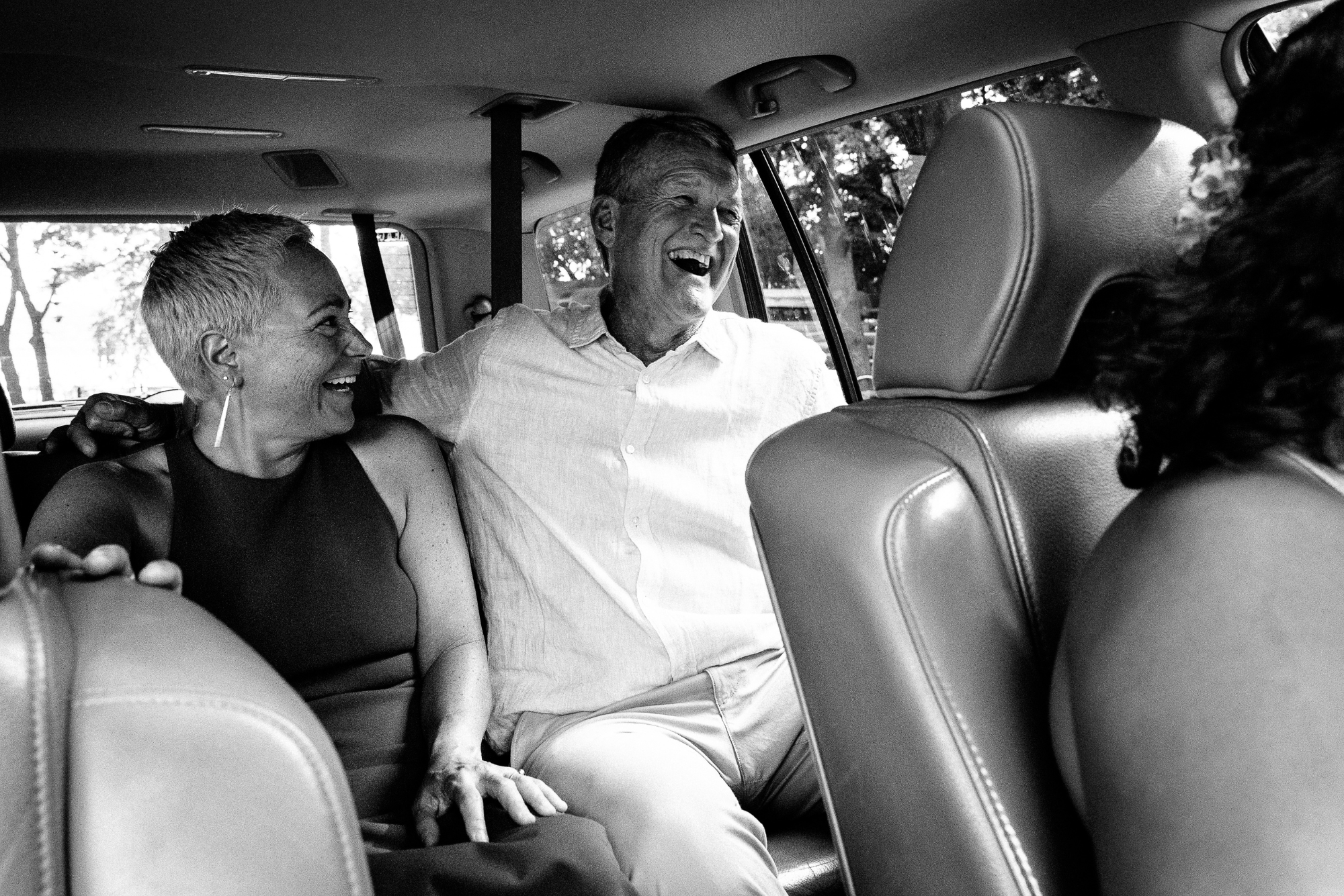 Four people, two women and two men, sitting inside a car, smiling and laughing, enjoying a happy moment together.