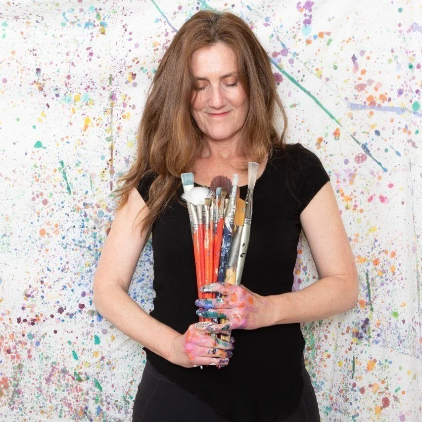 Person holding paintbrushes with paint-splattered background