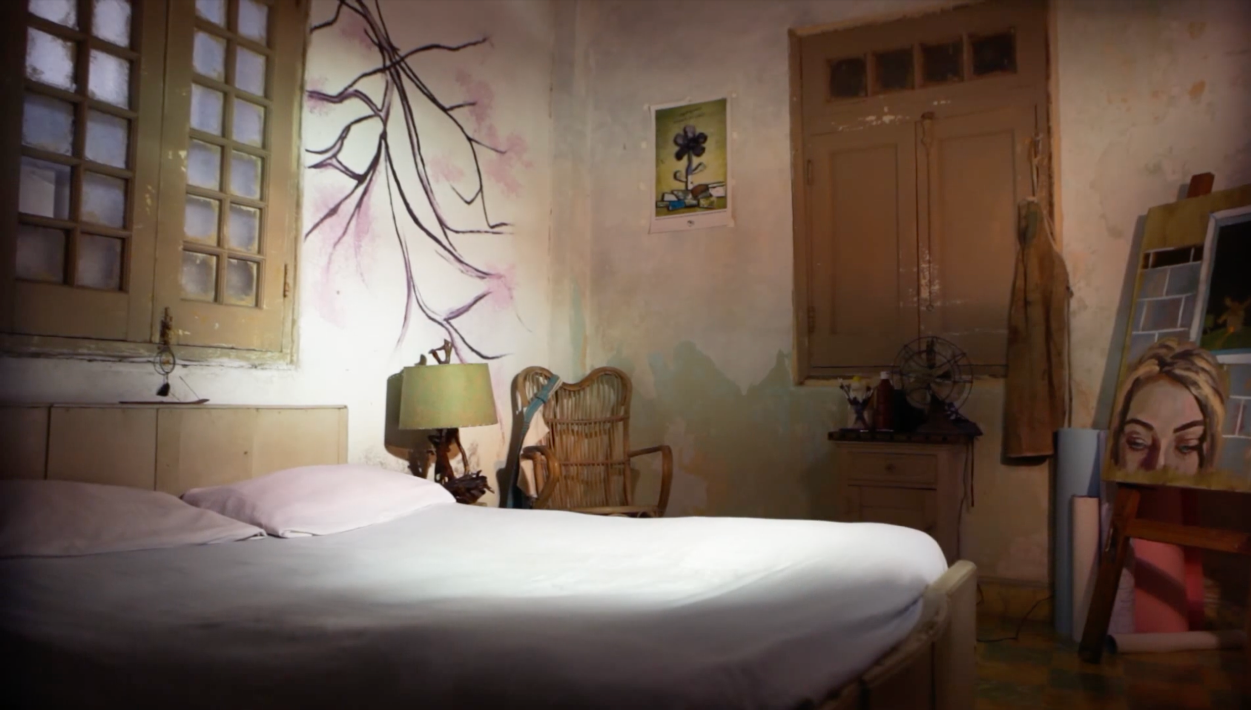 Patricia Machin Portfolio Designer Art director Miami A bedroom with a bed, wall murals including tree branches, a window, a wooden chair, a lamp, artwork on the walls, and studio art supplies.