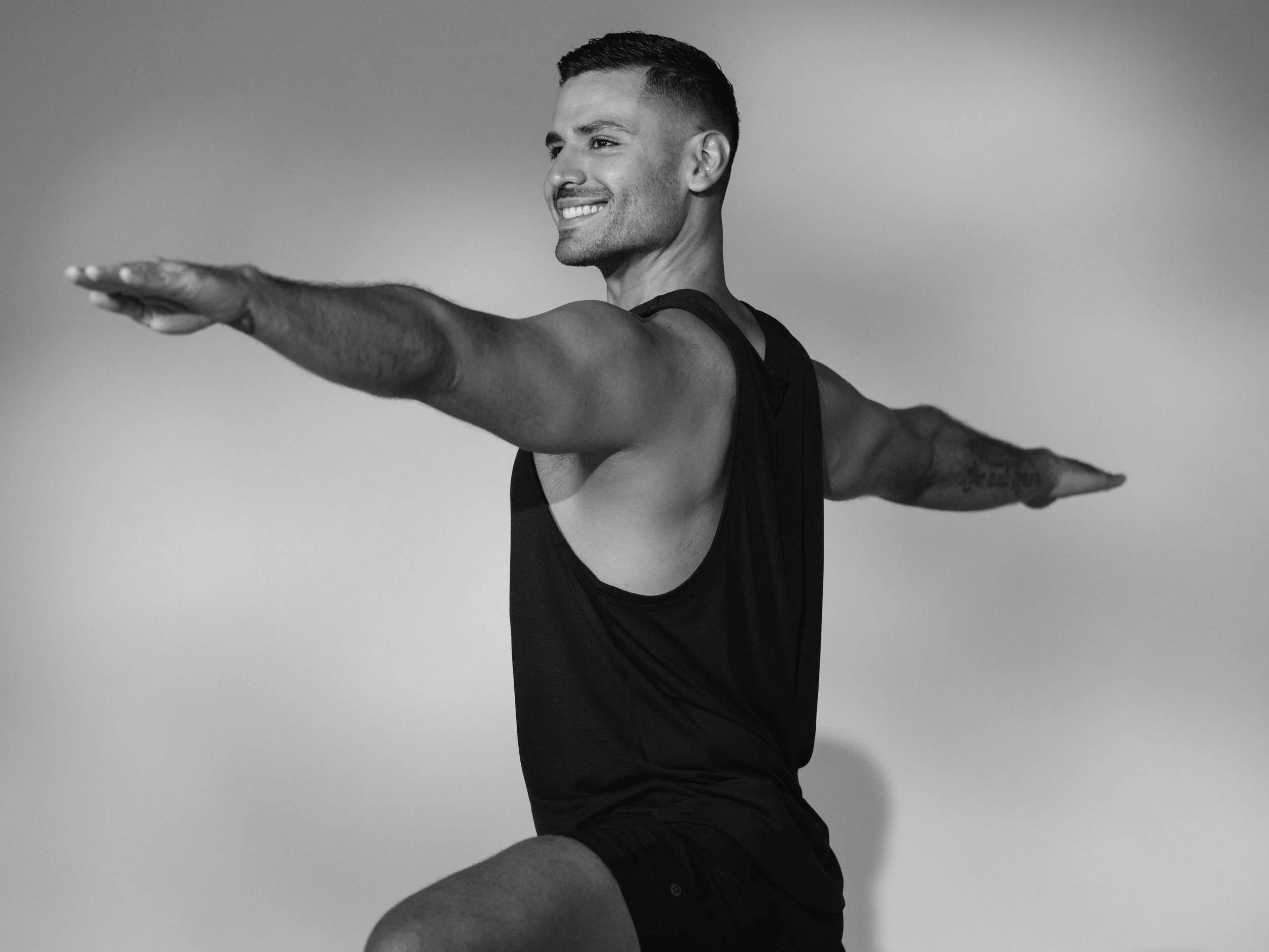 Patricia Machin Portfolio Designer and Art Director LEOM wellbeing Miami A smiling man with short hair performs a front balance pose, standing on one leg with arms extended and parallel to the ground.