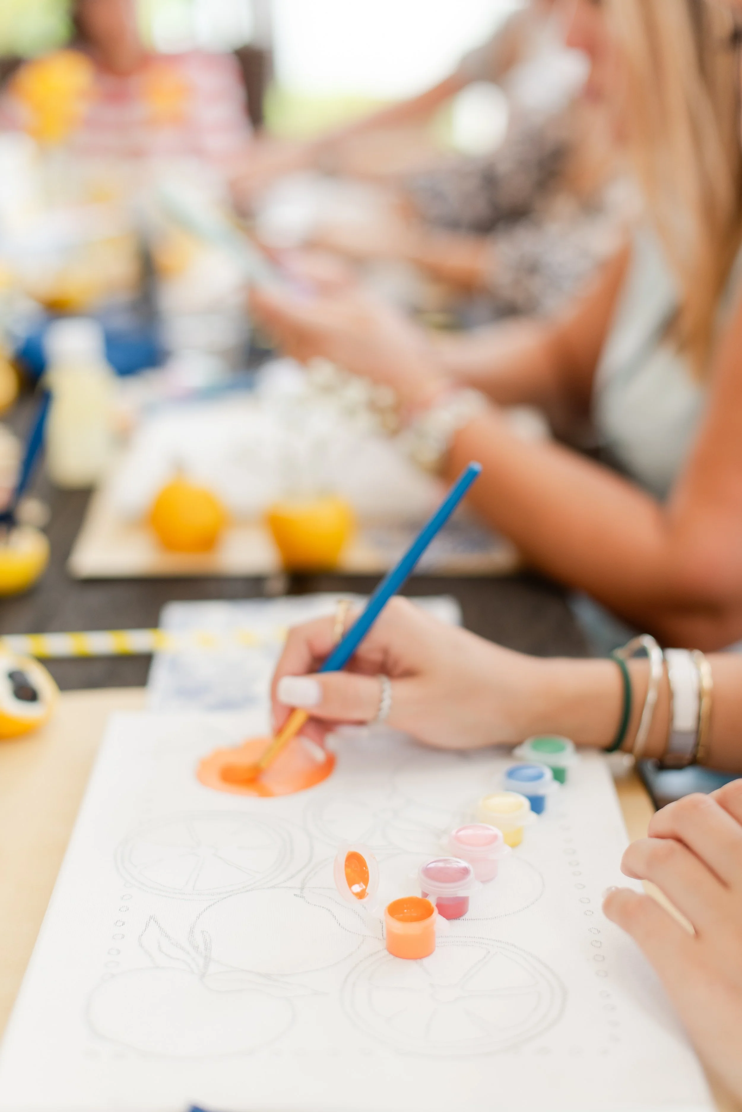 Patricia Machin Portfolio Designer and Art Director Muse&Flow Miami Paint kits People painting and decorating orange Halloween pumpkins with paint and brushes at a table.